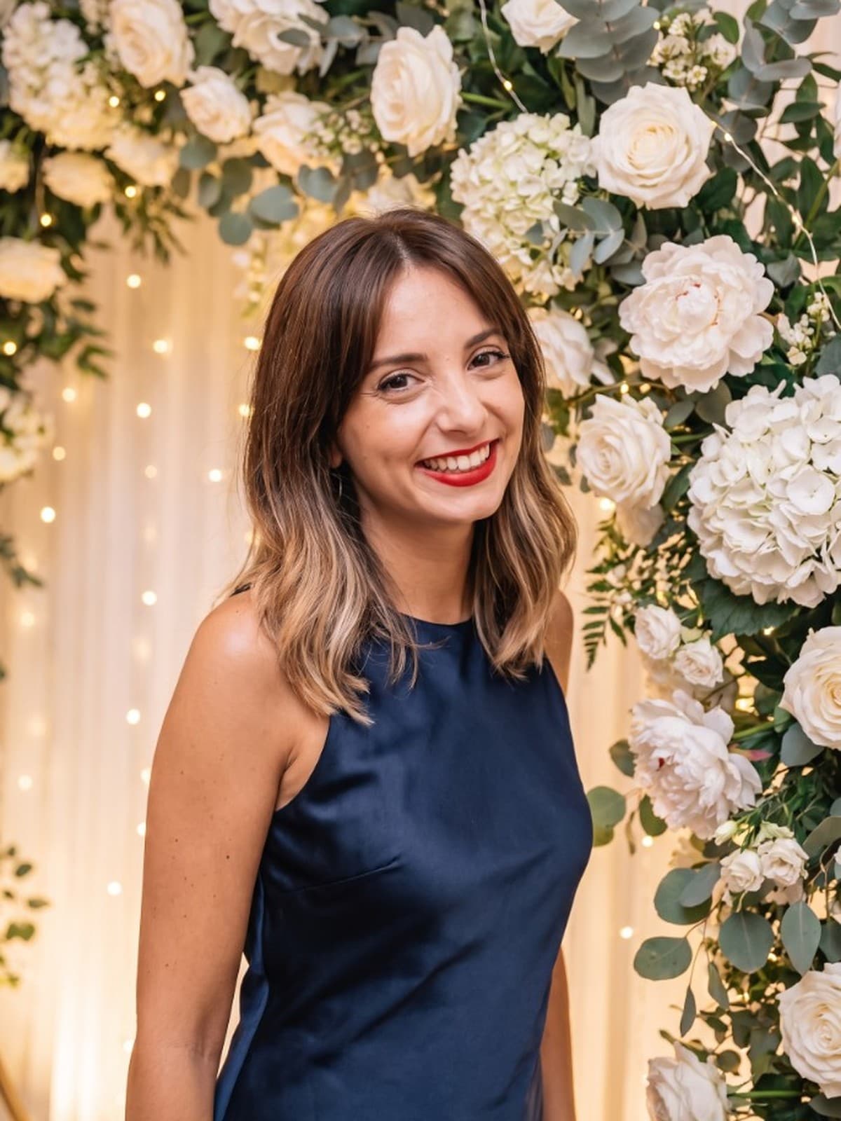 Nine, wedding planner de l’agence Ainsi soit fête, souriante devant une arche fleurie